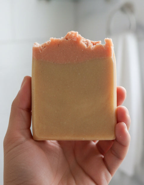 Hand holding a goat milk soap with pink clay and lavender essential oil