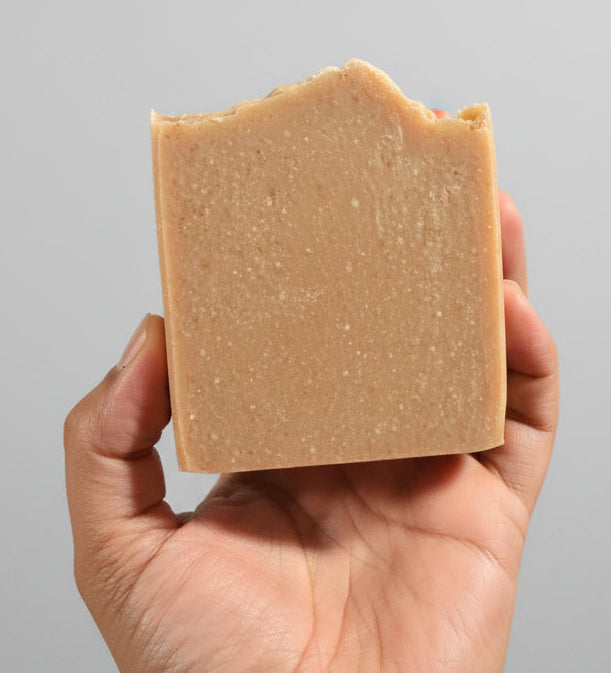 Hand holding a square piece of brown soap with a cluttered background