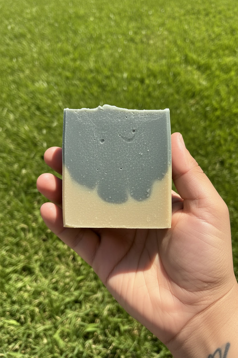 Hand holding a bar of soap with a grass background