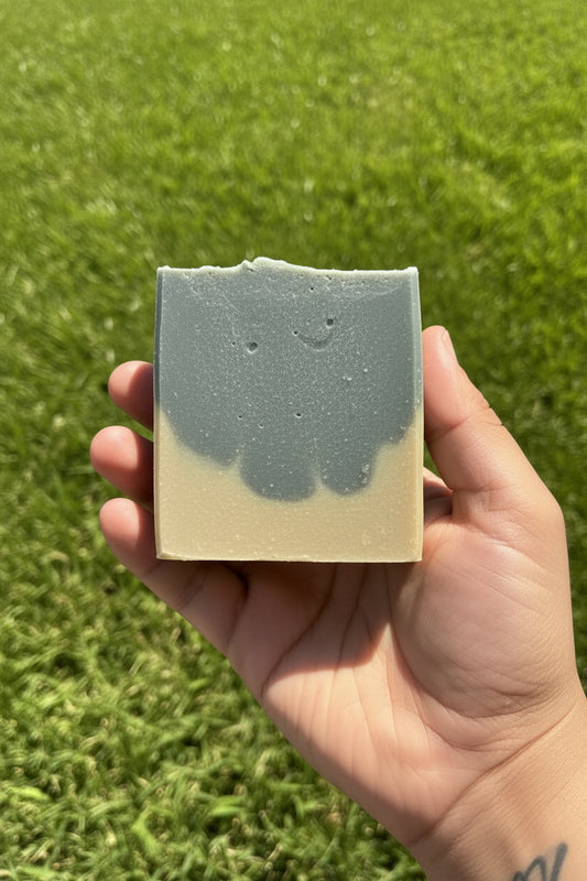 Hand holding a bar of soap with a grass background